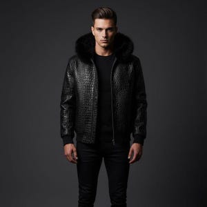 Könnte beinhalten: Schwarze Lederjacke mit Kapuze aus Kunstfell. Die Jacke hat ein strukturiertes, krokodilartiges Muster und einen Reißverschluss. Die Person trägt eine schwarze Hose und ein schwarzes Oberteil.