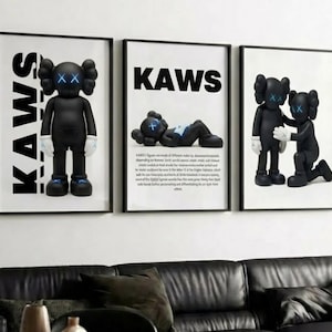 Op de afbeelding: Drie ingelijste kunstdrukken met zwarte KAWS-figuren met X-vormige ogen. De prints bevatten het woord "KAWS" in vette witte letters. Eén figuur staat, één ligt en één knielt.