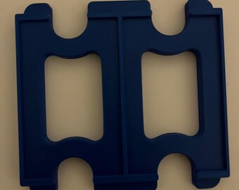 May include: A solid blue plastic object with two rectangular openings and a symmetrical design. The object has a series of curved and straight edges, with a flat base and rounded corners. The object is likely a tool or a component.