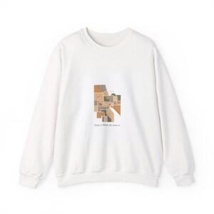 May include: A white sweatshirt with a geometric map design in brown, tan, and green. The text "Home is Where the Heart Is" is printed below the map. The sweatshirt has a crew neck and long sleeves.