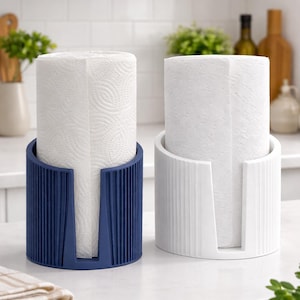 May include: Two paper towel holders, one navy blue and one white, each holding a roll of white paper towels. The holders have a modern design with vertical lines and a cutout for dispensing.