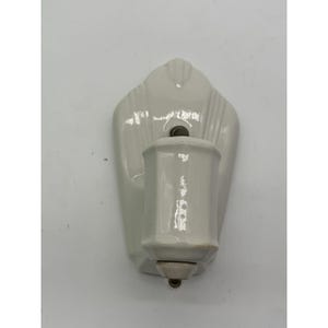 May include: A white ceramic wall-mounted fixture featuring a vertical, elongated backplate with subtle, raised linear detailing and a central, cylindrical, faceted projection extending outward, designed for functional utility.
