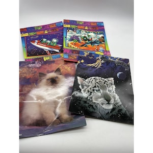 Puede incluir: Cuatro carpetas escolares vintage con ilustraciones coloridas. Una carpeta presenta un cohete con la marca Coca-Cola y personajes de dibujos animados. Otras carpetas muestran un gato esponjoso, un leopardo de las nieves y una escena invernal.