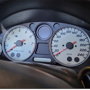 Peut inclure: Tableau de bord de voiture avec compteurs. Le compteur de vitesse affiche jusqu'&agrave; 240 km/h. Le compte-tours indique jusqu'&agrave; 8 x1000r/min. D'autres jauges affichent les niveaux de carburant et la temp&eacute;rature. Les cadrans sont blancs avec des aiguilles rouges.