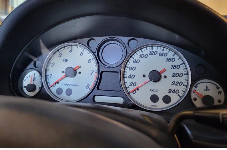 Peut inclure: Tableau de bord de voiture avec compteurs. Le compteur de vitesse affiche jusqu'&agrave; 240 km/h. Le compte-tours indique jusqu'&agrave; 8 x1000r/min. D'autres jauges affichent les niveaux de carburant et la temp&eacute;rature. Les cadrans sont blancs avec des aiguilles rouges.