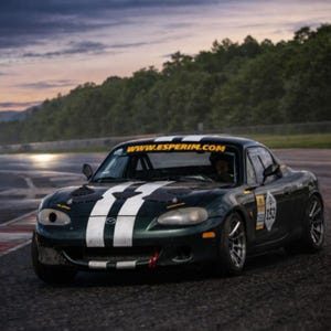 Może przedstawiać: Ciemnozielony samochód sportowy z białymi pasami wyścigowymi i napisem "WWW.ESPERIM.COM" na przedniej szybie. Samochód ma numer wyścigowy i znajduje się na torze wyścigowym. Widoczne są reflektory samochodu.