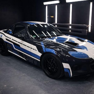 Può includere: Un'auto sportiva nera, bianca e blu dal design elegante. L'auto ha un profilo ribassato, ruote nere e un design a strisce da corsa. Il testo "ELECTRAXIS" è visibile sul cofano.