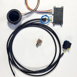 Peut inclure: Ensemble de composants &eacute;lectroniques, comprenant une jauge circulaire noire, un bo&icirc;tier noir avec plusieurs fils, un petit potentiom&egrave;tre et un c&acirc;ble noir. Divers fils color&eacute;s sont regroup&eacute;s. Les composants sont dispos&eacute;s sur une surface blanche.