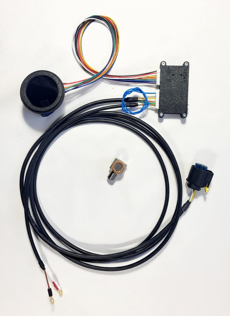 Peut inclure: Ensemble de composants &eacute;lectroniques, comprenant une jauge circulaire noire, un bo&icirc;tier noir avec plusieurs fils, un petit potentiom&egrave;tre et un c&acirc;ble noir. Divers fils color&eacute;s sont regroup&eacute;s. Les composants sont dispos&eacute;s sur une surface blanche.