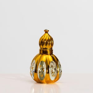 May include: A decorative, gold-colored perfume bottle with an ornate design. The bottle has a bulbous body with a ribbed, dome-shaped top. The clear glass sections of the bottle are decorated with gold-colored floral patterns.