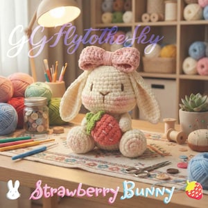 Op de afbeelding: Een handgemaakte gehaakte konijn met een roze strik en een aardbei. Het konijn is crèmekleurig met roze accenten en houdt een rood-groene aardbei vast. De tekst "Strawberry Bunny" staat onderaan de afbeelding.
