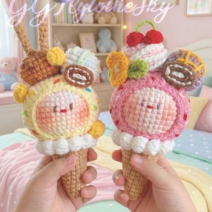 Może przedstawiać: Dwa ręcznie robione rożki lodów na szydełku, jeden żółty i jeden różowy, trzymane w dłoniach. Lody mają urocze buzie i są ozdobione różnymi dodatkami. Widoczny jest tekst "GG FlytotheSky" i "Kawaii Ice Cream Dango".