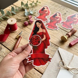 May include: A die-cut sticker featuring an illustration of a person with long dark hair wearing a red off-the-shoulder gown and a matching veil, holding a large bouquet of red roses, with a blank red banner at the bottom for custom text.
