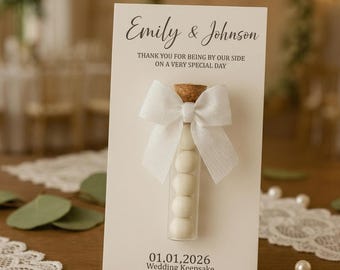May include: A wedding keepsake card with the names "Emily & Johnson" printed at the top. The card features a small glass vial filled with white candies, tied with a white bow. The text "THANK YOU FOR BEING BY OUR SIDE ON A VERY SPECIAL DAY" is printed below the names.