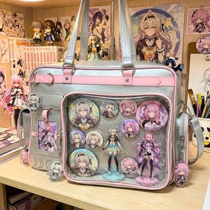 May include: A silver and pink anime-style school bag, adorned with character badges and charms. The bag features a clear front pocket showcasing various character pins and figurines. The bag is on a wooden surface, with other anime-related items in the background.