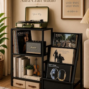 May include: A black metal tiered storage unit holding a green portable record player, a Marshall speaker, vinyl records by The Beatles, Fleetwood Mac, and Daft Punk, books including Vogue and Kinfolk, a small violin model, and two storage boxes.