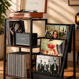 May include: A dark brown wooden record storage shelf with a black metal frame. The top shelf holds an orange portable record player with the text "Years stay" inside the lid and a black speaker. The lower shelves contain vinyl records.
