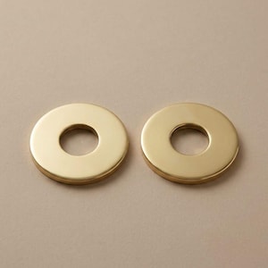 May include: Two gold-colored, circular metal objects with a hole in the center. The objects are evenly spaced and have a smooth, reflective surface. The background is a solid, neutral color.