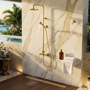 May include: A gold shower system with a round overhead rainfall head and a handheld sprayer, mounted on a white marble wall. A white towel with the letters V.C. embroidered on it rests on a small shelf next to a brown bottle of liquid soap.