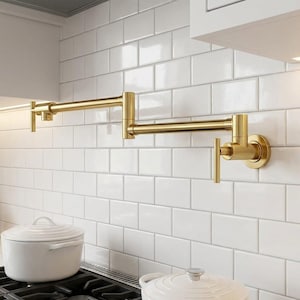 May include: A wall-mounted, gold-toned pot filler faucet featuring a double-jointed, articulating swing arm design with two control handles. The fixture is constructed with a metallic finish and is positioned horizontally against a white tiled wall.