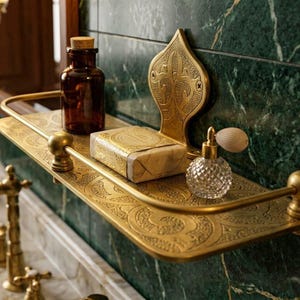 May include: A decorative brass shelf with ornate detailing holds a brown glass bottle, a bar of soap, and a crystal perfume bottle. The shelf is mounted on a green marble wall, creating a vintage bathroom aesthetic.