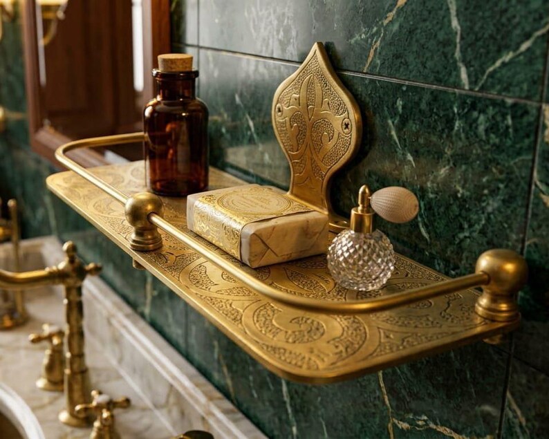 May include: A decorative brass shelf with ornate detailing holds a brown glass bottle, a bar of soap, and a crystal perfume bottle. The shelf is mounted on a green marble wall, creating a vintage bathroom aesthetic.
