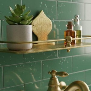 May include: A brass-colored shelf with a small succulent in a white pot, decorative gold accent, and glass bottles. The shelf is mounted on a green tiled wall, creating a stylish bathroom or spa aesthetic.