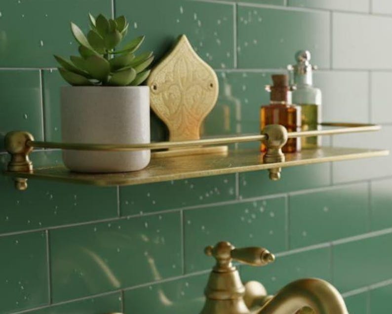 May include: A brass-colored shelf with a small succulent in a white pot, decorative gold accent, and glass bottles. The shelf is mounted on a green tiled wall, creating a stylish bathroom or spa aesthetic.
