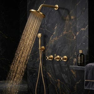 May include: A brushed gold shower system featuring a large circular rainfall showerhead, a handheld shower wand with a flexible hose, and three cross-handle control valves. Water flows from the main showerhead in a steady stream.