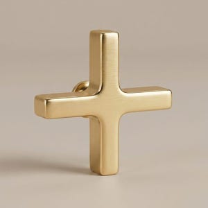 May include: A gold-coloured cross with a matte finish. The cross has a simple, classic design with a square shape on each end. The cross is a religious symbol.