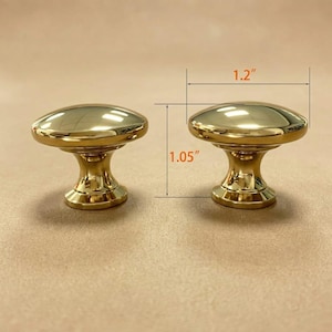 May include: Two polished gold-tone metal cabinet knobs with a smooth, rounded top and a tapered base. The knobs are shown with dimension lines indicating a width of 3.05 cm and a height of 2.67 cm for the hardware piece.