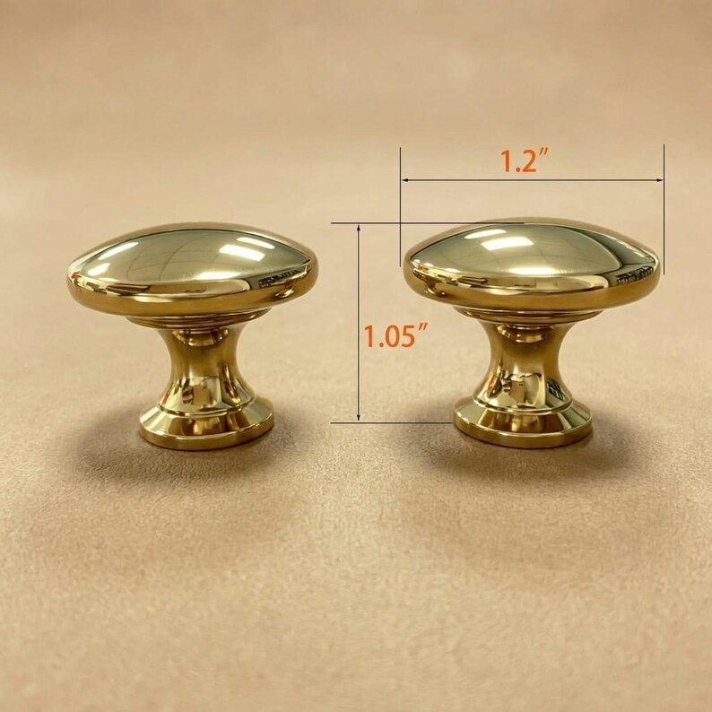 May include: Two polished gold-tone metal cabinet knobs with a smooth, rounded top and a tapered base. The knobs are shown with dimension lines indicating a width of 3.05 cm and a height of 2.67 cm for the hardware piece.