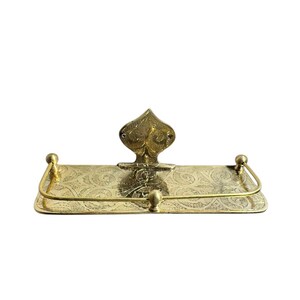 May include: A vintage brass shelf with an ornate design. The shelf has a rectangular base with a curved front and a decorative backplate. The brass has a warm, golden hue and is embellished with floral patterns.