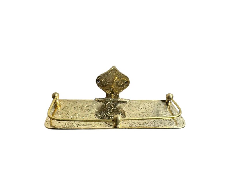 May include: A vintage brass shelf with an ornate design. The shelf has a rectangular base with a curved front and a decorative backplate. The brass has a warm, golden hue and is embellished with floral patterns.
