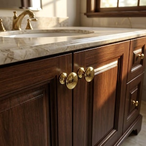 May include: A dark wood bathroom vanity cabinet featuring polished gold round knobs on the doors and drawers. The vanity is topped with a light beige marble countertop and includes a gold faucet fixture positioned above the integrated sink basin.