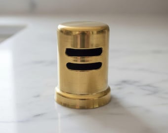 May include: A cylindrical brass shaker with a polished metallic finish. The object features two horizontal, elongated rectangular slots positioned on the upper front side, allowing for the dispensing of contents from within the container.