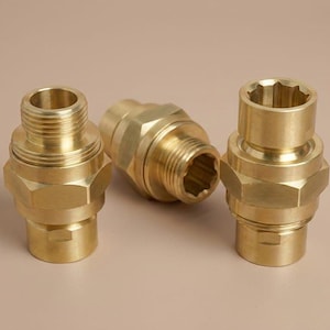 May include: Three brass plumbing fittings are displayed against a neutral backdrop. Each fitting features a threaded end, a hexagonal body, and a socket end with an internal star-shaped design. The brass has a shiny, metallic finish.