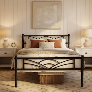 May include: A black metal bed frame with a decorative headboard and footboard. The bed is made up with white bedding and several orange and cream-colored pillows. Two white nightstands with lamps flank the bed. A woven basket sits under the bed.