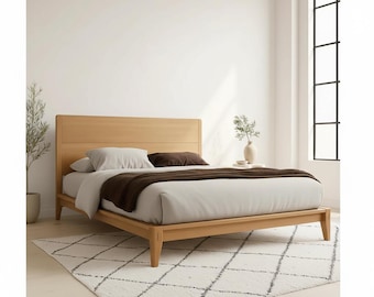 May include: A light wood bed frame with a headboard, featuring a light gray duvet, brown throw blanket, and pillows. The bed is on a white rug with a geometric pattern. A vase with greenery sits on a side table.