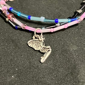 May include: A multi-strand bracelet featuring pink, blue, and clear beads. A silver fairy charm dangles from the bottom strand. The bracelet is on a dark surface.