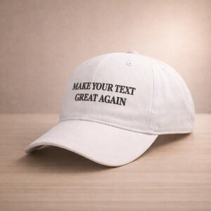 May include: White baseball cap with the text "MAKE YOUR TEXT GREAT AGAIN" in black. The cap is made of a soft material and has a curved brim. The hat is sitting on a wooden surface.