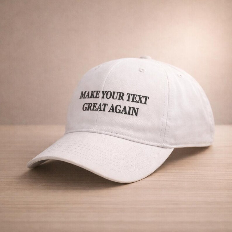 May include: White baseball cap with the text "MAKE YOUR TEXT GREAT AGAIN" in black. The cap is made of a soft material and has a curved brim. The hat is sitting on a wooden surface.