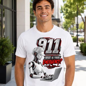 May include: A white short-sleeved t-shirt featuring a graphic print of a white and red robotic figure typing on a laptop. Above the figure, the number 911 is printed in large grey text, with the red text "WHAT IS YOUR EMERGENCY?" below it.