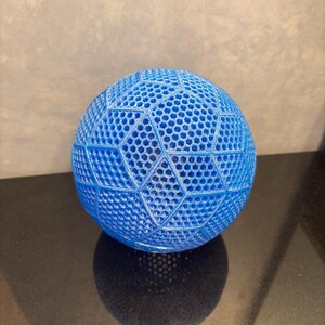 May include: A bright blue spherical object featuring a complex, three-dimensional geometric lattice structure. The surface is composed of repeating hexagonal patterns arranged within larger triangular and diamond-shaped segments, creating a textured, open-work design.