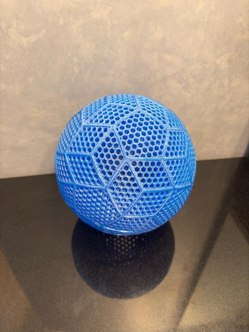 May include: A bright blue spherical object featuring a complex, three-dimensional geometric lattice structure. The surface is composed of repeating hexagonal patterns arranged within larger triangular and diamond-shaped segments, creating a textured, open-work design.