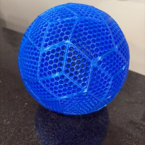 May include: A bright blue spherical object featuring a complex, three-dimensional honeycomb lattice structure. The surface is composed of interconnected hexagonal cells arranged in a geometric pattern, creating a semi-transparent, open-work design.