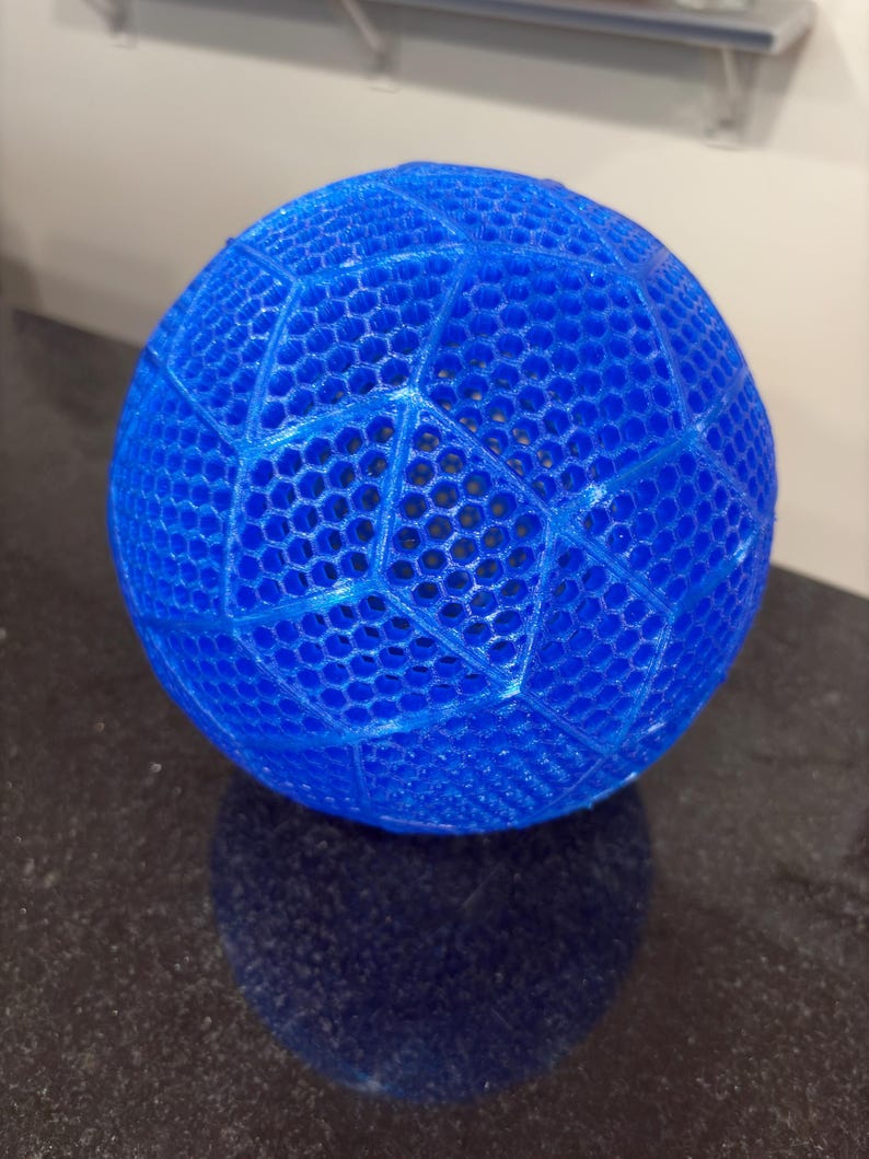 May include: A bright blue spherical object featuring a complex, three-dimensional honeycomb lattice structure. The surface is composed of interconnected hexagonal cells arranged in a geometric pattern, creating a semi-transparent, open-work design.