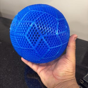 May include: A bright blue spherical object featuring a complex, three-dimensional lattice structure with a repeating hexagonal pattern across its entire surface. The ball has a semi-translucent appearance and a textured, grid-like finish.