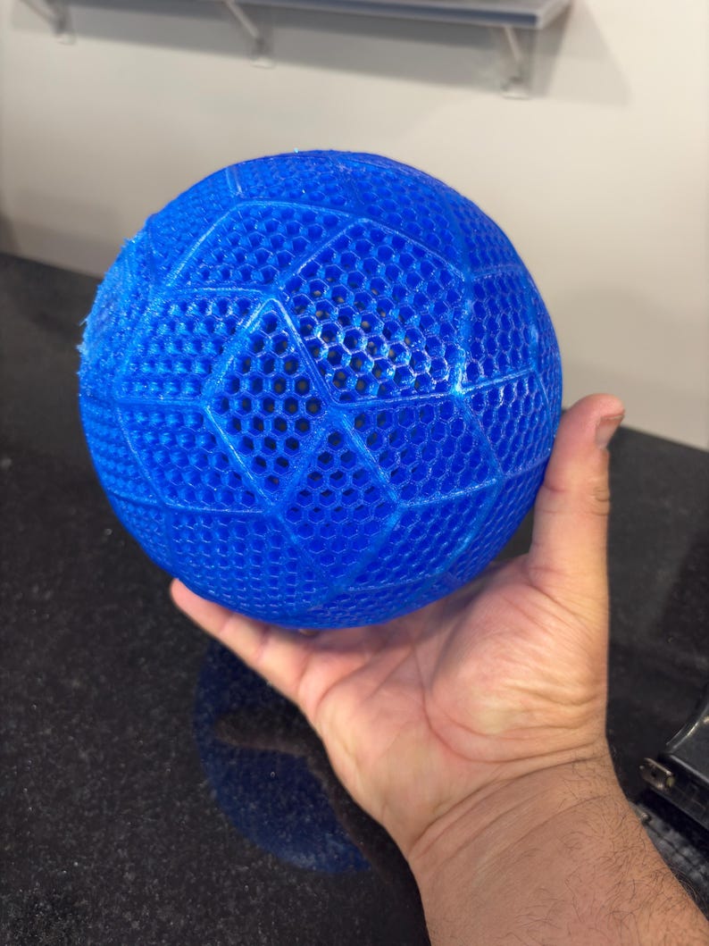 May include: A bright blue spherical object featuring a complex, three-dimensional lattice structure with a repeating hexagonal pattern across its entire surface. The ball has a semi-translucent appearance and a textured, grid-like finish.