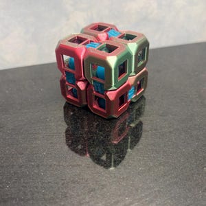 May include: A multi-colored, geometric cube with a complex, open design. The cube features a combination of red, green, and blue hues, creating a visually striking effect. The cube is made of a series of interconnected, open-faced squares.